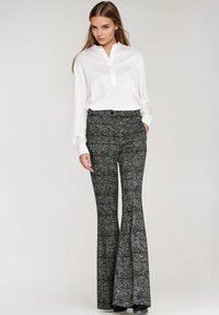 Biała koszula z długim rękawem i kołnierzykiem, zestawiona z rozkloszowanymi czarno-białymi spodniami o fakturowanym, wzorzastym wzorze.