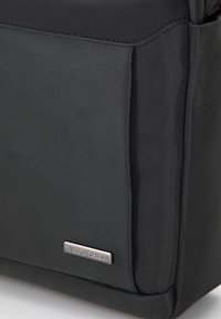 Borsa nera in nylon con superficie testurizzata e dettagli lisci. Presenta una piastrina con logo metallico, forma strutturata e scomparto laterale.