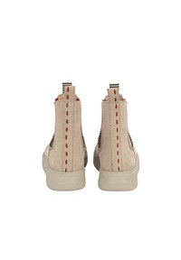 Beżowe zamszowe botki za kostkę z czerwonymi przeszyciami, teksturowanym tylnym panelem i białą gumową podeszwą. Zawierają pętle ułatwiające zakładanie.