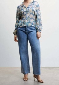 Blouse en voile à motif floral bleu clair, accompagnée d'un jean bleu taille haute et jambe droite avec des bords effilochés, agrémentée de talons nus.