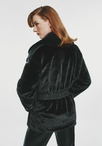 Czarny płaszcz z sztucznego futra z szerokim kołnierzem i teksturowanym paskiem w talii. Posiada długie rękawy oraz gładkie, błyszczące wykończenie.