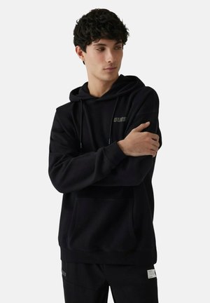 Felpa con cappuccio nera in materiale morbido con tasca frontale, cappuccio con coulisse e piccolo dettaglio logo. Presenta polsini e orlo a coste.