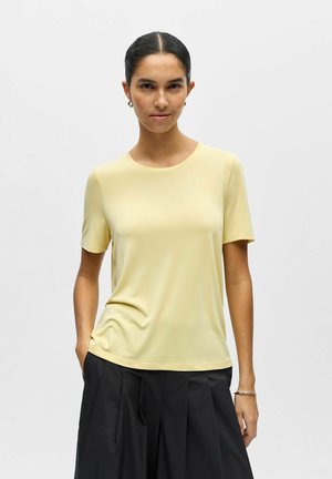 T-shirt manches courtes jaune clair en tissu lisse, avec un col rond et une coupe décontractée, associé à une jupe plissée noire.