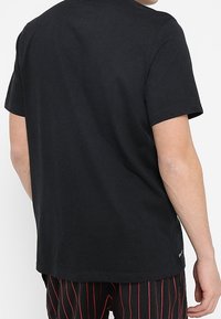 Camiseta de algodón negra con cuello redondo, mangas cortas y un ajuste relajado. Presenta un diseño limpio sin patrones ni texto visibles.