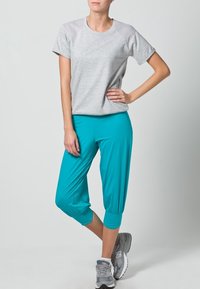 T-shirt gris clair à manches courtes et encolure dégagée, associé à un pantalon capri teal avec un ourlet froncé, porté avec des baskets grises.