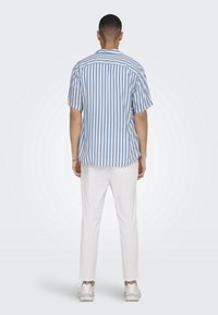 Hellblau- und weiß gestreiftes Kurzarmhemd mit lässigem Schnitt, kombiniert mit weißen Hosen und hellen Sneakers, von hinten betrachtet.