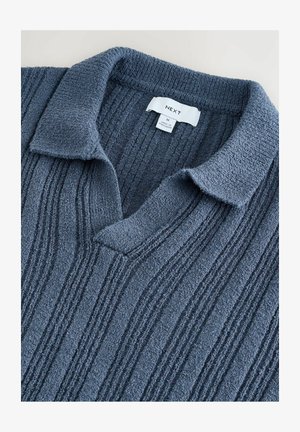 Pull en maille texturée bleu marine avec un décolleté en V et un design avec col. Présente des motifs en côtes verticales et une étiquette en tissu indiquant la marque et la taille.