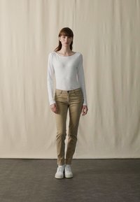 Ljusgrå långärmad topp kombinerad med beige tajta byxor och vita sneakers. Enkel design, slät textur, inga mönster eller utsmyckningar.