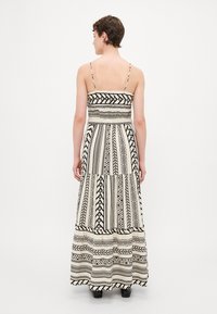Rochie maxi de culoare crem cu modele geometrice negre, bretele reglabile, bust ajustat și fustă cu straturi.