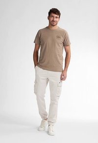 Béžové bavlněné tričko s kulatým výstřihem a logem na levé straně hrudi, doplněné bílými nákladními kalhotami s kapsami a elastickými manžetami.