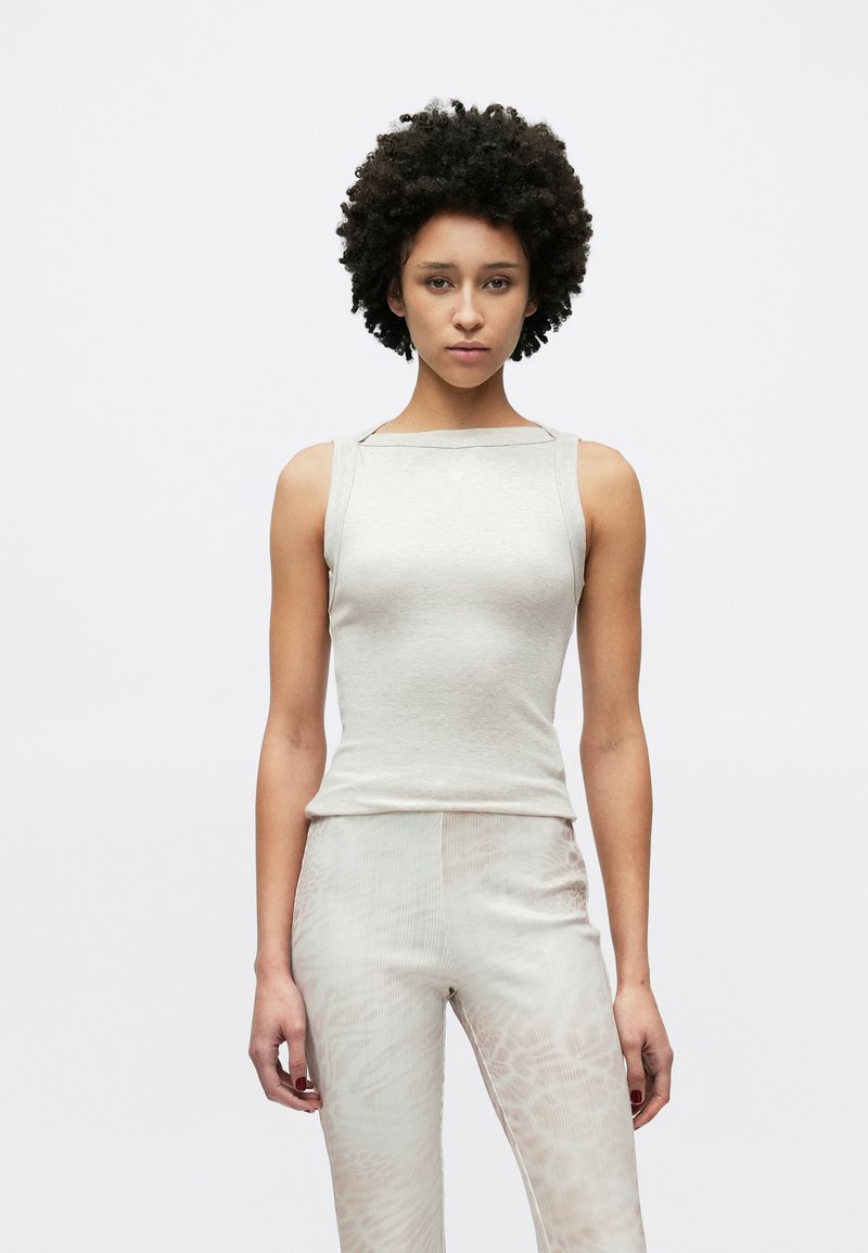 Top grigio chiaro senza maniche con un design aderente. Tessuto liscio, scollo quadrato e dettagli discreti sulle spalle. Abbinato a pantaloni chiari con motivo.