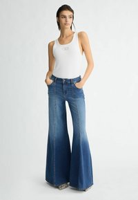 Valge ribidega tank topp, millel on ümar kaelus, koos siniste laia lõikega teksadega, mis sisaldavad taskuid ja denimitekstiuri kontrastsete õmblustega.