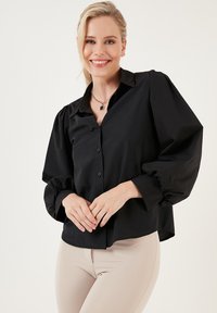 Black button-up shirt with puffed sleeves, made of smooth fabric. Features a classic collar and a slightly cropped fit.