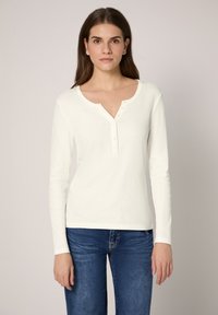 Witte top met lange mouwen, een ronde halslijn en een gedeeltelijke knoopsluiting. Zacht materiaal en een aansluitend ontwerp, gecombineerd met donkerblauwe jeans.