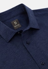Mörkblå bomullsskjorta med en texturerad yta, med en spetsig krage, framknäppning och varumärkesetikett på kragen.