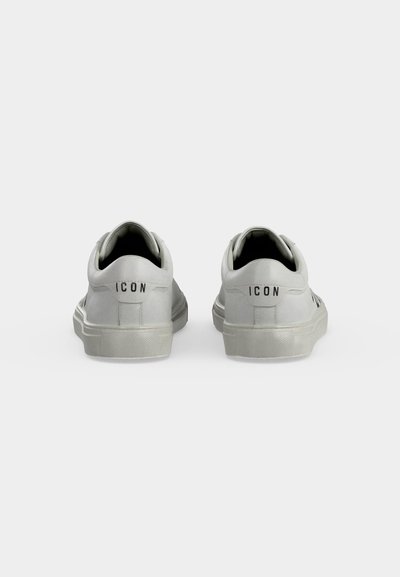 Paire de baskets basses blanches vues de dos, affichant le texte "ICON" sur la zone du talon de chaque chaussure.