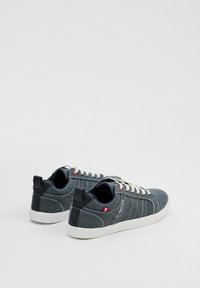 Zapatillas de denim en azul oscuro con cordones blancos, talón y acentos en negro contrastante, con líneas cosidas y un pequeño detalle de logo.