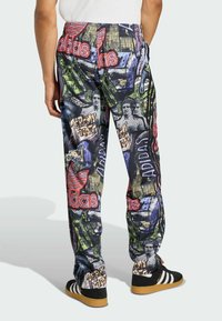 Adidas-Hosen mit einem bunten Muster in Blau, Grün und Rot. Die Grafiken zeigen Logos, Figuren und städtische Wahrzeichen. Gummibund.