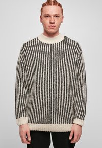 Pull en tricot avec des rayures verticales noires et blanches, un col rond et des poignets côtelés. Texture douce avec une coupe ample.