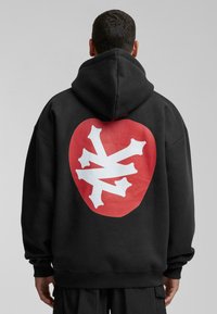 Schwarzer Hoodie mit einem großen roten Grafiken auf der Rückseite und einem weißen abstrakten Design; aus weichem, strukturiertem Gewebe gefertigt.
