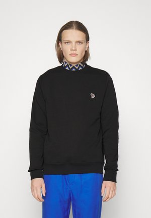 Sort sweatshirt med rund hals og ribbede ærmer, med et lille broderet logo på brystet. Kombinationen er med blå bukser.