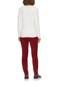 Weißes, geripptes Langarmoberteil, kombiniert mit roten, schmal geschnittenen Hosen, die eine glatte Textur aufweisen, sowie lässigen Sneakers mit einer Plateausohle.