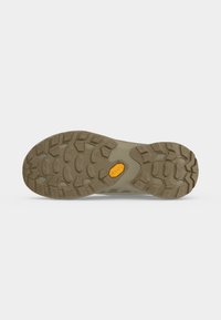 Semelle d'une chaussure de randonnée marron avec des crampons profonds pour l'adhérence et un logo Vibram jaune au centre.