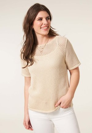 Beige gebreid T-shirt met korte mouwen en een mesh ontwerp, ronde halslijn en geribbelde manchetten. Gestyleerd met witte broeken met een ontspannen pasvorm.