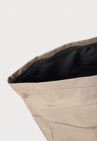 Sac en tissu beige avec une texture lisse et un intérieur noir, présentant des coutures visibles le long de l'ouverture et une forme douce.