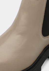 Beež nahast pahkluu saapad sileda tekstuuriga ja musta elastse paneeliga külgedel. Kummi tald, kus on nähtavad õmblused.