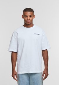 White cotton t-shirt with a crew neck and short sleeves; features "ASPIRE AND ACHIEVE" printed in dark blue on the left side.