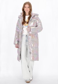 Irideszcens hosszú puffernadrág kapucnival, steppelt részekkel és bordás mandzsettákkal. Fehér felső és világos színű farmer nadrág felett viselt.