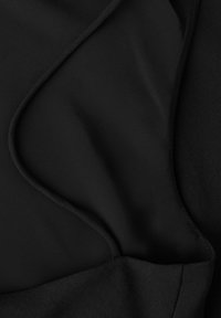 Musta kangas, jossa on sileitä ja teksturoiduja osia, esittäen kaarevan sauman yksityiskohdan ja kerroksittaisia laskoksia.