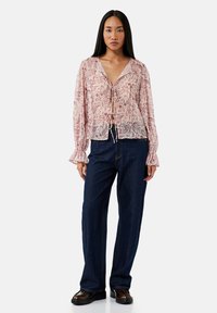 Lichtroze blouse met paisleypatroon, v-hals en striksluiting. Lange, puffed mouwen met opgeknopte manchetten. Gecombineerd met donkerblauwe wijde jeans.