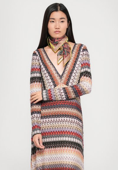 Ilgųjų rankovių megztas suknelė, pagaminta iš įvairių spalvų dryžių, su giliu V formos kaklu, tekstūruotu audiniu ir atitinkančia raštuotą skarelę, surišta aplink kaklą.