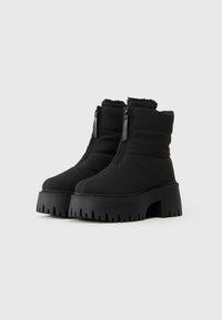 Botas de tobillo aisladas negras con dos cremalleras, suela de plataforma gruesa y textura acanalada. Tela suave con detalles acolchados en la parte superior.