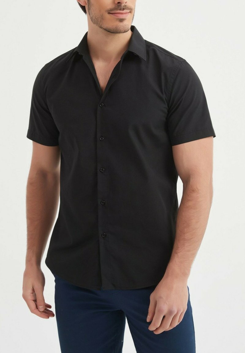 Chemise noire à manches courtes, en coton uni, avec un col pointu et une coupe droite, dotée de six boutons sur le devant.