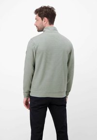 Zielona prążkowana bluza z kołnierzem typu stójka, charakteryzująca się subtelną teksturą, długimi rękawami i luźnym krojem. Czarny detal z logo na ramieniu.