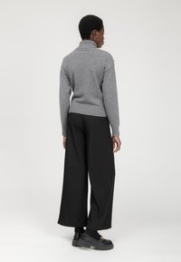 Maglione grigio a maglia con colletto e orlo a coste ampie, abbinato a pantaloni neri a gamba larga e scarpe nere robuste. Design semplice e minimalista.