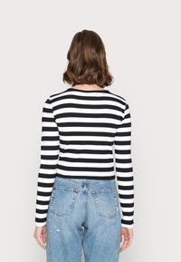 Schwarz-weißer, gestreifter Langarmoberteil; körpernahe Passform mit Rundhalsausschnitt. Kombiniert mit hellblauen, ausgeblichenen Jeans.