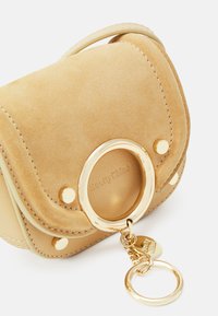 Piccola borsa in suede beige con hardware dorato, dotata di un anello arrotondato e portachiavi. Cuciture dettagliate e logo all'interno testurizzato.