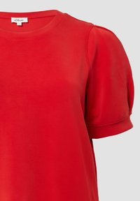 Rode katoenen t-shirt met korte pofmouwen, ronde halslijn en een zachte textuur, met zichtbare stiksels aan de rand van de mouwen.