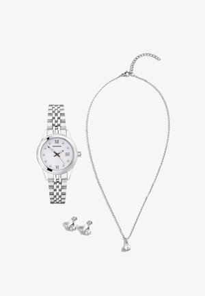 Montre en acier inoxydable argenté avec cadran blanc, marqueurs en cristal, bracelet à maillons, associée à des boucles d'oreilles argentées et un collier en chaîne avec un pendentif transparent.