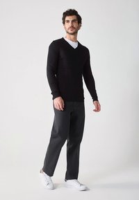 Schwarzer, gerippter Langarmpullover, figurbetontes Design, kombiniert mit dunkelgrauer Hose und weißen Turnschuhen. Schlichter, lässiger Stil mit V-Ausschnitt.