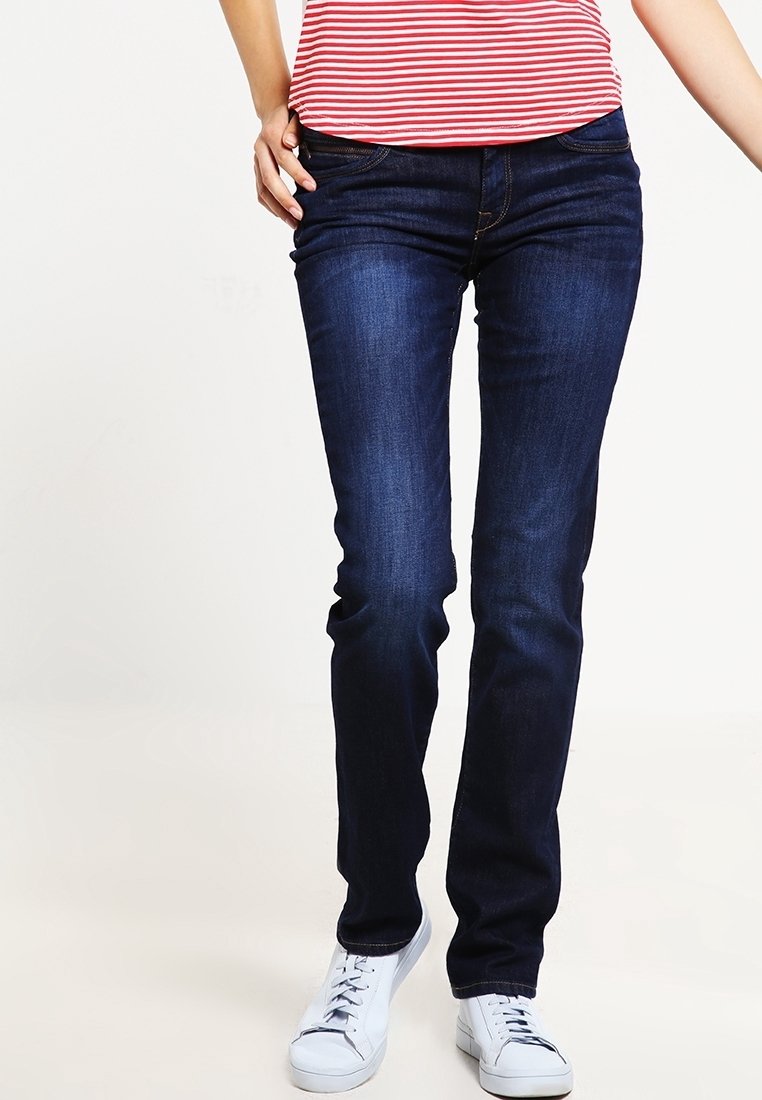 Jeans in denim blu scuro con una vestibilità slim, dotati di un classico design a cinque tasche e dettagli di cucitura discreti. Abbinati a sneakers bianche.