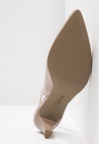 Chaussure à talon haut beige reposant sur le côté, montrant une semelle pointue avec grip texturé et le nom de la marque Gabor embossé.