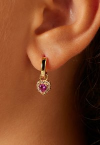 Gouden oorbel in hartvorm met een centrale roze edelsteen omringd door kleine heldere steentjes, bevestigd met een eenvoudige ophaaksluiting.