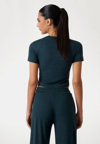 Teal cropped top met korte mouwen, gecombineerd met een bijpassende losvallende broek. Zachte textuur en elastische tailleband zijn zichtbaar vanaf de achterkant.