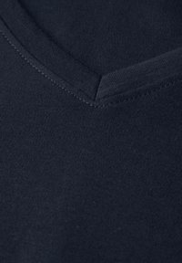 Tričko s v-výstřihem v tmavě námořnické barvě, které se vyznačuje hladkou strukturou a jemným šitím podél výstřihu.