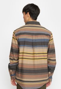 Meerkleurig gestreept shirt in bruin, blauw, geel en oranje, met een kraag, lange mouwen en knoopdetails op de manchetten. Gedetailleerde stof.